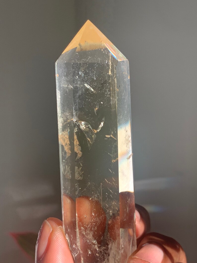 May include: A clear quartz crystal point with a light brown tip. The crystal is faceted and has a smooth, polished finish.