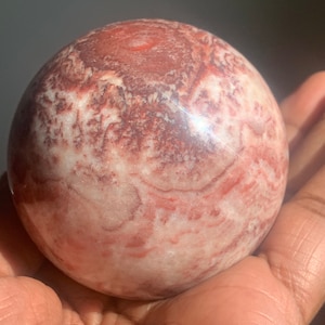 May include: A large, polished sphere of red and white banded jasper. The sphere has a smooth, glossy finish and is a beautiful example of this type of stone.