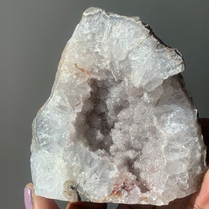 K&ouml;nnte beinhalten: Ein wei&szlig;er und violetter Geode mit einer gro&szlig;en &Ouml;ffnung, die die Kristallformationen im Inneren freilegt.