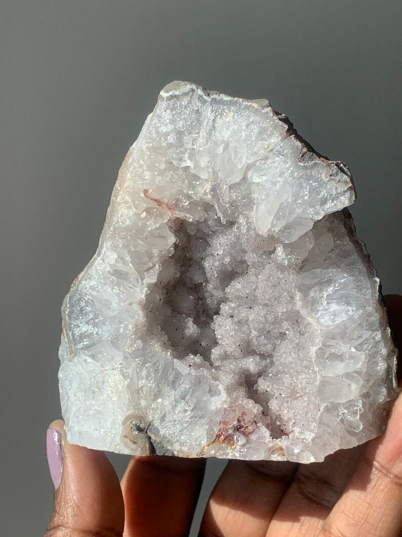 K&ouml;nnte beinhalten: Ein wei&szlig;er und violetter Geode mit einer gro&szlig;en &Ouml;ffnung, die die Kristallformationen im Inneren freilegt.
