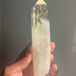 Pode incluir: Uma ponta de cristal de quartzo transparente com uma ponta amarela. O cristal &eacute; segurado em uma m&atilde;o e &eacute; parcialmente transl&uacute;cido, permitindo que a luz passe por ele. O cristal &eacute; de cor amarelo p&aacute;lido e tem uma apar&ecirc;ncia natural e n&atilde;o polida.