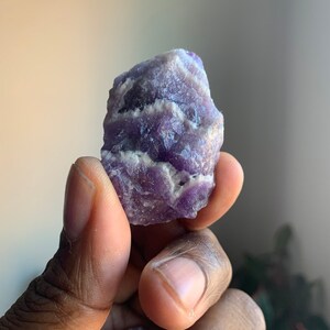 Könnte beinhalten: Ein violetter Amethyst-Kristall mit weißen Streifen und einer rauen, natürlichen Textur.