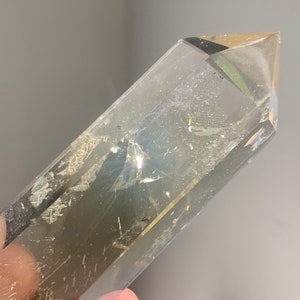 May include: A clear quartz crystal point with a smoky brown hue. The crystal is faceted and has a pointed tip. The crystal is approximately 5 inches long.