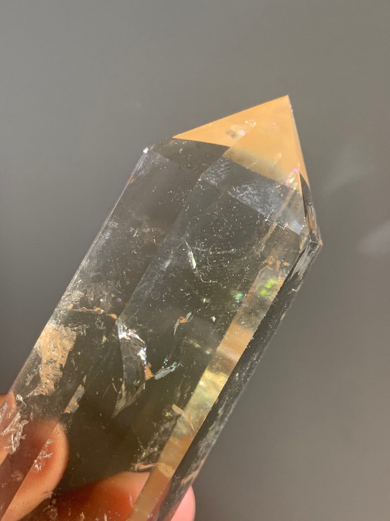 May include: A clear quartz crystal point with a golden brown hue. The crystal is faceted and has a pointed tip. The crystal is approximately 5 inches long.
