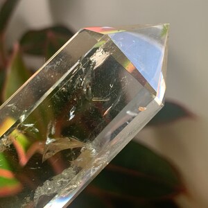 May include: A clear quartz crystal point with a natural, raw texture. The crystal is pointed at the top and has a smooth, polished base.