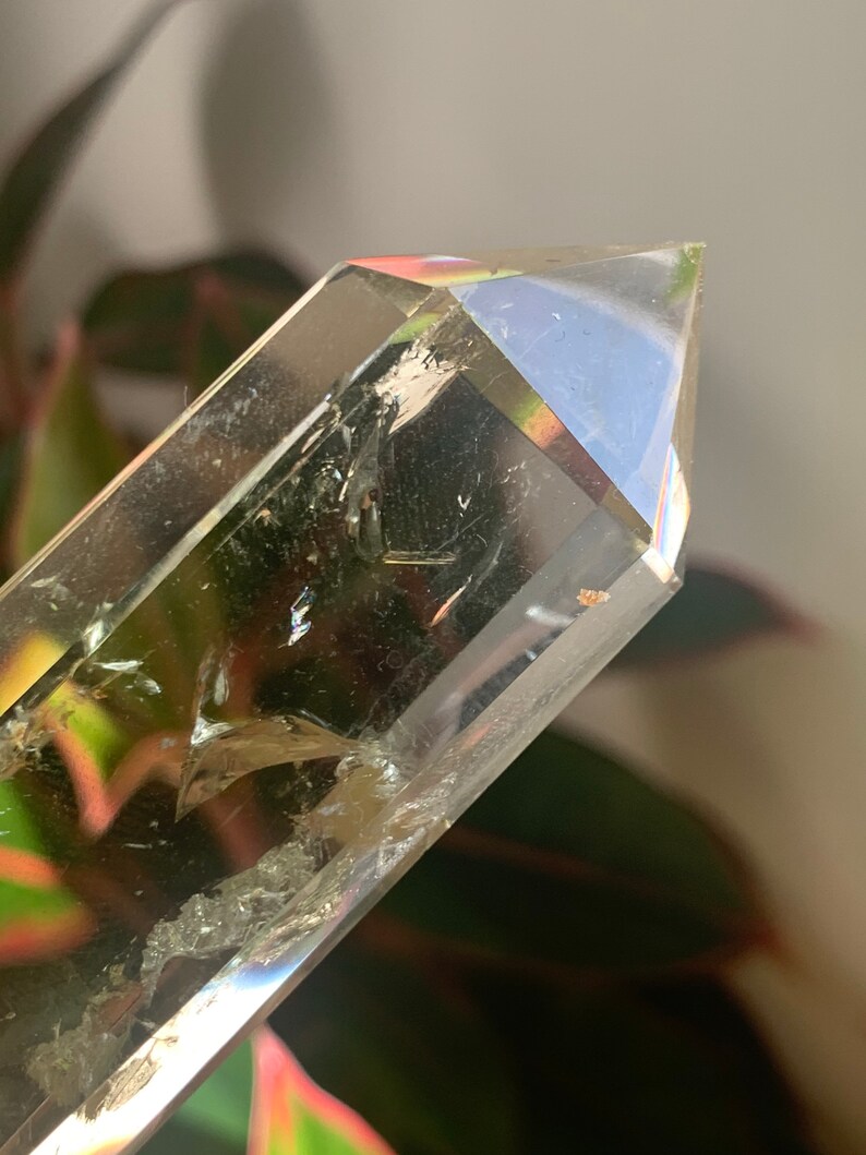 May include: A clear quartz crystal point with a natural, raw texture. The crystal is pointed at the top and has a smooth, polished base.