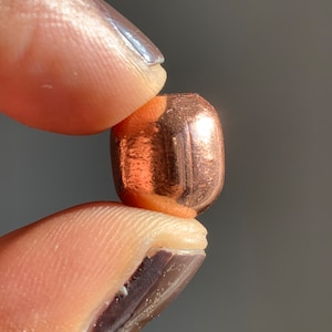 May include: A single copper bead with a smooth, shiny surface. The bead is round and has a slightly flattened shape.