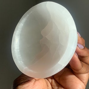 May include: A white selenite bowl with a smooth, polished surface. The bowl is slightly curved and has a natural, organic shape.