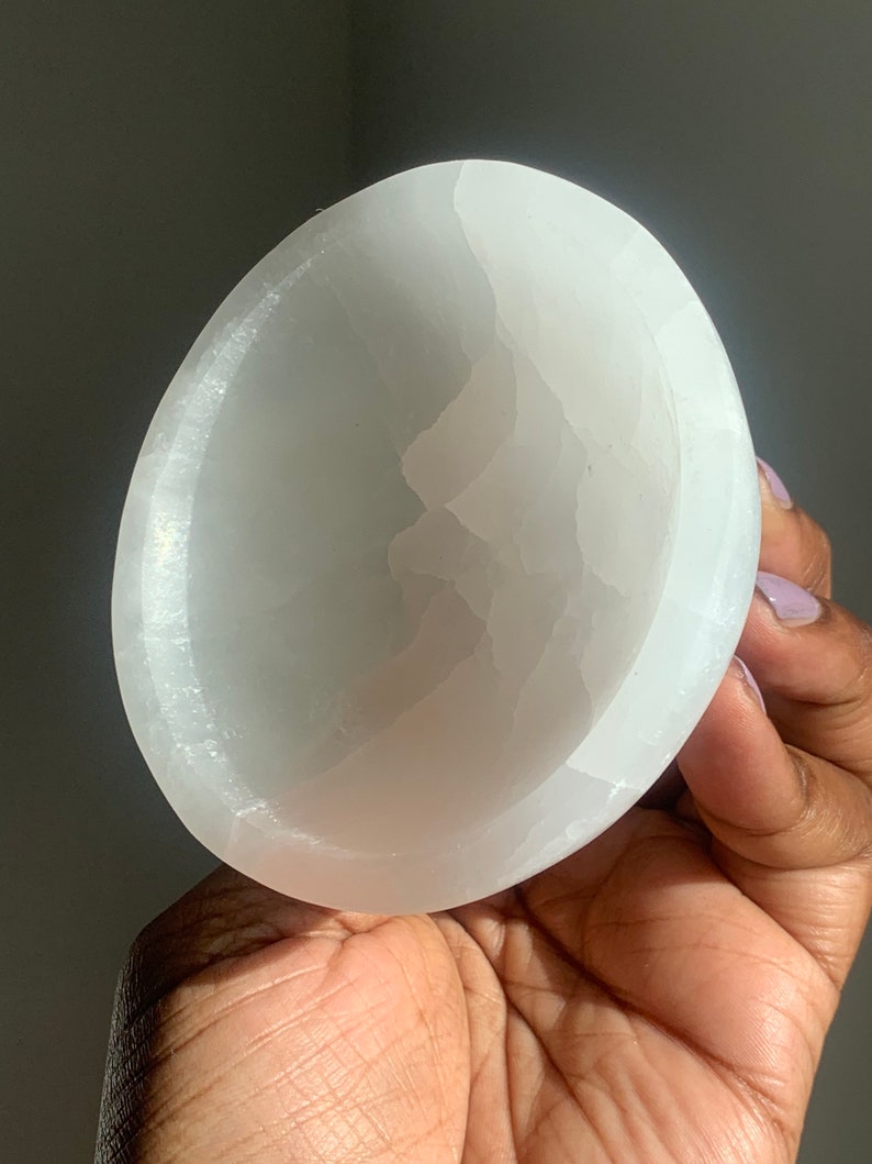 May include: A white selenite bowl with a smooth, polished surface. The bowl is slightly curved and has a natural, organic shape.