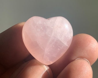 May include: A heart-shaped pink rose quartz crystal. The crystal is smooth and polished, with a light pink color.