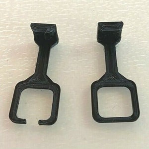 May include: Two black plastic hooks with a square opening at the bottom. The hooks are designed to hang items on a wall or other surface.