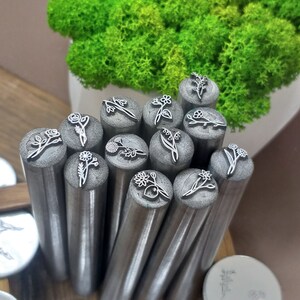 Puede incluir: Un conjunto de 14 herramientas de estampado de flores de metal con diferentes dise&ntilde;os florales. Las herramientas est&aacute;n dispuestas en c&iacute;rculo y est&aacute;n listas para ser utilizadas para estampar.