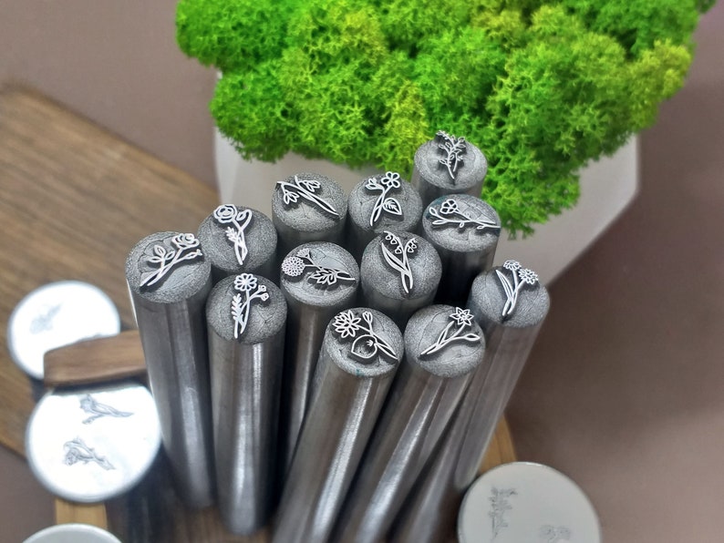 Puede incluir: Un conjunto de 14 herramientas de estampado de flores de metal con diferentes dise&ntilde;os florales. Las herramientas est&aacute;n dispuestas en c&iacute;rculo y est&aacute;n listas para ser utilizadas para estampar.