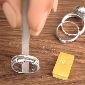 May include: Two silver rings with a textured design, one with a round top, and a gold bar with a crown design on top.