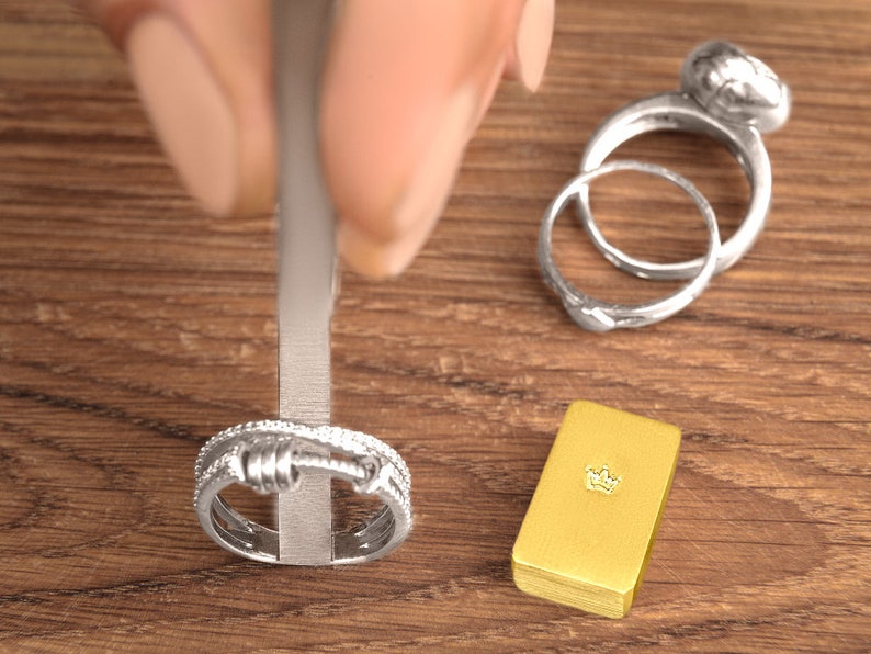 May include: Two silver rings with a textured design, one with a round top, and a gold bar with a crown design on top.