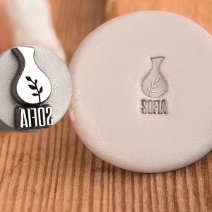 May include: A close-up of two metal stamps. The stamp on the left has the word "SOFIA" engraved on it. The stamp on the right has a vase with a plant inside and the word "SOFIA" engraved on it.