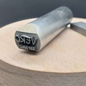 May include: A silver metal stamp with the text "VERO CERAMICS" engraved on the side.
