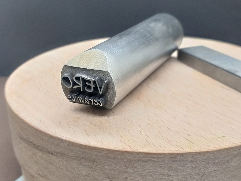 May include: A silver metal stamp with the text "VERO CERAMICS" engraved on the side.