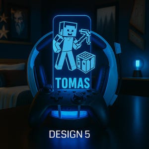 May include: A blue-lit gaming lamp featuring a Minecraft character design, the name "TOMAS", and the text "DESIGN 5". The lamp is set on a black controller base, with a headset behind it.