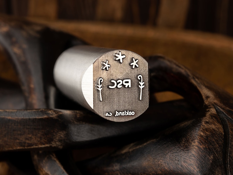 Pu&ograve; includere: Un timbro in metallo argentato con il testo "R2C" e un design a stella. Il testo "oakland, ca" &egrave; anche inciso sul timbro.