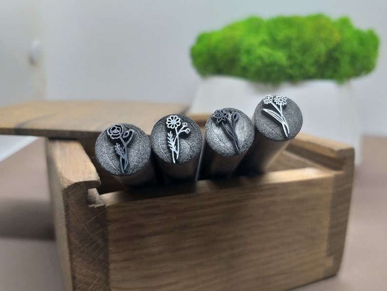 Puede incluir: Cuatro sellos de metal con dise&ntilde;os florales en una caja de madera. Los sellos son plateados y tienen diferentes dise&ntilde;os de flores, incluyendo una margarita, un narciso y una rosa.