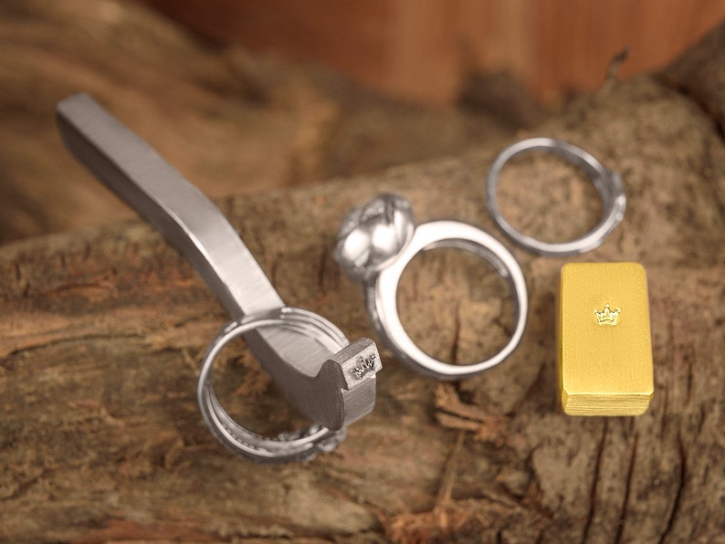 May include: A silver ring sizing tool with a silver ring and a gold ring with a crown design on a wooden surface.