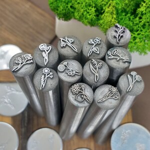 Puede incluir: Un conjunto de 13 herramientas de estampado de flores de metal con diferentes dise&ntilde;os florales. Los sellos est&aacute;n dispuestos en un c&iacute;rculo sobre una superficie de madera.