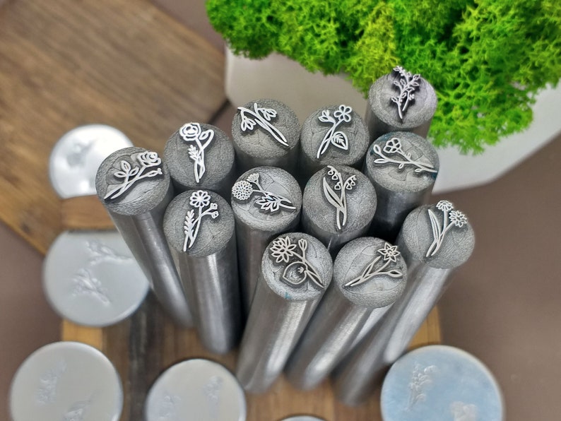 Puede incluir: Un conjunto de 13 herramientas de estampado de flores de metal con diferentes dise&ntilde;os florales. Los sellos est&aacute;n dispuestos en un c&iacute;rculo sobre una superficie de madera.
