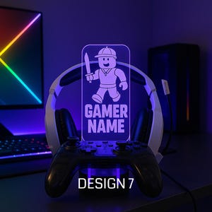 May include: A gaming-themed LED lamp with a cartoon character holding a sword, the words "GAMER NAME," and "DESIGN 7." The lamp is set on a stand with a game controller and headphones.