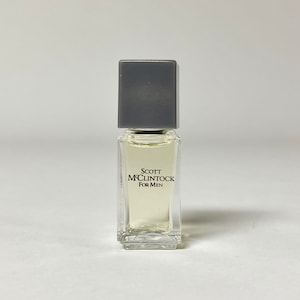 May include: A small clear glass bottle of cologne with a gray square cap. The label reads "Scott McLintock For Men".