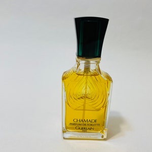 May include: A clear glass bottle of Chamade perfume by Guerlain. The bottle has a green and black cap and a gold label with the text "Chamade Parfum de Toilette Guerlain Paris".