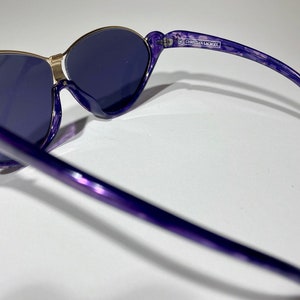 May include: Purple and gold sunglasses with a Christian Lacroix label on the arm.