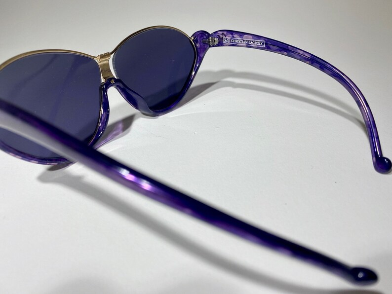 May include: Purple and gold sunglasses with a Christian Lacroix label on the arm.