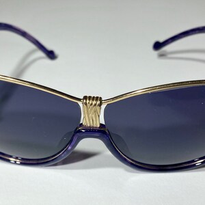 May include: Purple sunglasses with a gold metal frame and dark lenses.