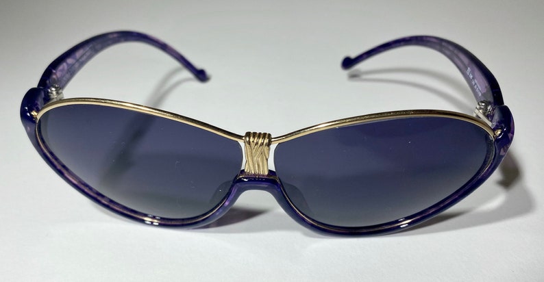 May include: Purple sunglasses with a gold metal frame and dark lenses.
