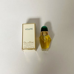 May include: A small bottle of Oscar de la Renta Volupté Eau de Toilette Natural Spray. The bottle is yellow with a green cap and a gold label. The label reads "Volupté" and "Oscar de la Renta Lau de Toilette Vaporisateur Naturel Natural Spray 10 ml 1/3 US. FL. OZ."