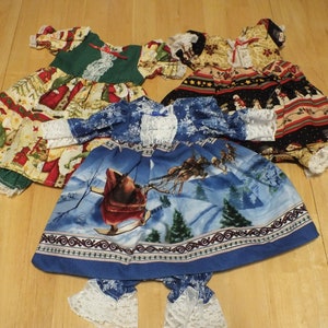 May include: Three Christmas-themed doll dresses. One dress is green and white with a red and white Santa Claus print. Another dress is blue and white with a winter scene featuring a sleigh and reindeer. The third dress is black, red, and white with a snowman and Santa Claus print.