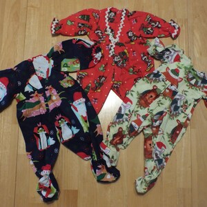 May include: Three pairs of Christmas pajamas for babies. One pair is red with a white trim and features a Mickey Mouse design. Another pair is green with a white trim and features a woodland animal design. The last pair is blue with a white trim and features a Santa Claus design.