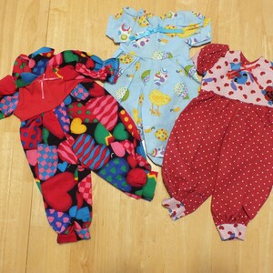 May include: Three doll outfits, one blue with a bird and egg pattern, one red with white polka dots, and one red with a heart and checkered pattern.
