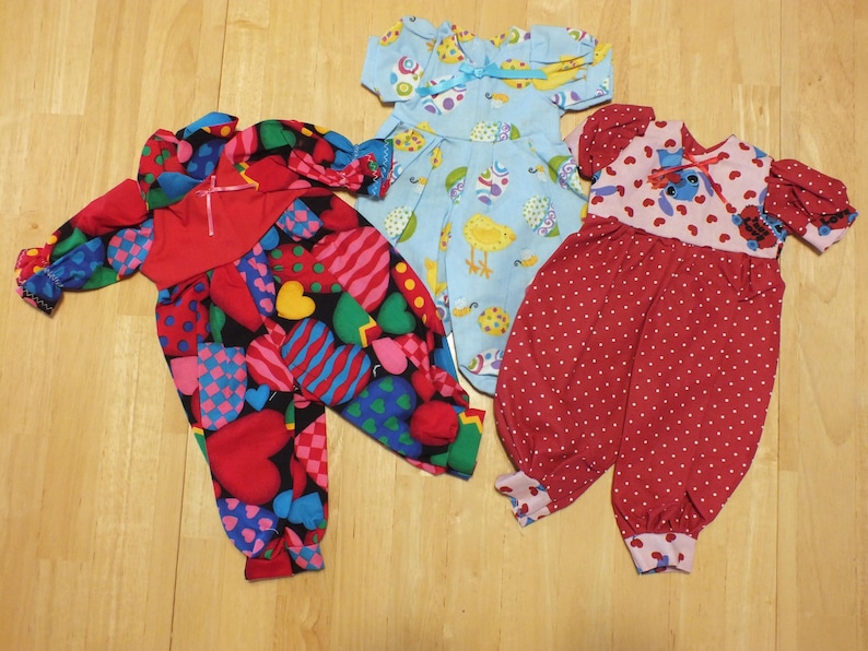 May include: Three doll outfits, one blue with a bird and egg pattern, one red with white polka dots, and one red with a heart and checkered pattern.