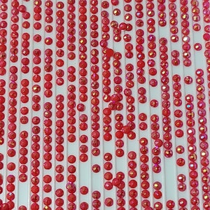 May include: A close-up image of a sheet of red iridescent rhinestones. The rhinestones are arranged in rows on a white background.