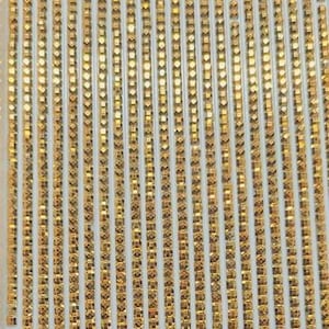 May include: A sheet of gold-colored adhesive rhinestones arranged in rows. Each rhinestone is square-shaped and has a faceted surface.