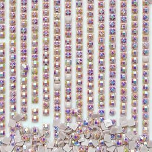 May include: Close-up of iridescent square and rectangular craft beads. The beads are arranged in vertical rows, with a mix of square and rectangular shapes. The colors shift with light, displaying hues of purple, yellow, and blue.