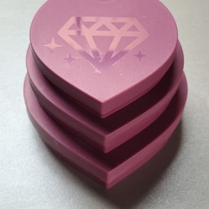 May include: Three stacked heart-shaped pink containers with a diamond design and glitter accents.
