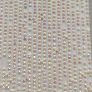 May include: A close-up image of a sheet of iridescent white rhinestones. The rhinestones are arranged in rows on a white background.