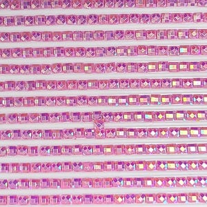 May include: Rows of small, square, pink iridescent rhinestones. The rhinestones are arranged in straight lines, creating a textured, sparkling surface. The color shifts between pink and other colors.