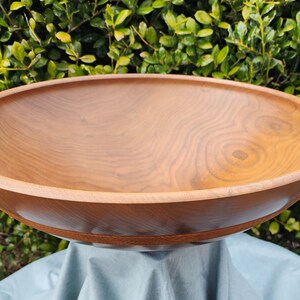 May include: A large, wooden bowl with a natural wood finish. The bowl is made of light brown wood with a grain pattern. The bowl is sitting on a blue cloth.