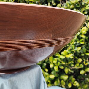 May include: A large, brown wooden bowl with a decorative, carved rim. The bowl is sitting on a blue cloth.