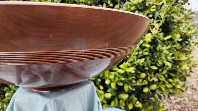 May include: A large, brown wooden bowl with a decorative, carved rim. The bowl is sitting on a blue cloth.