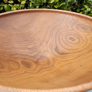 May include: A large, wooden bowl with a natural, light brown finish. The bowl is made of wood with a beautiful grain pattern.